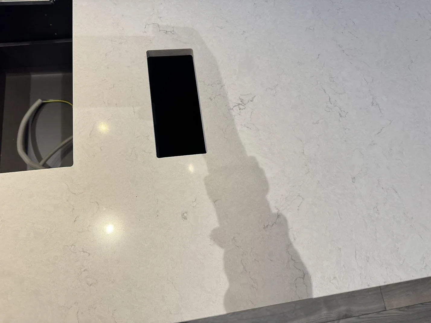 Närbild på den polerade ytan i Silestone Snowy Ibiza med mjuk grå ådring och en infälld bänkkontakt i en köksö i Klippan.
