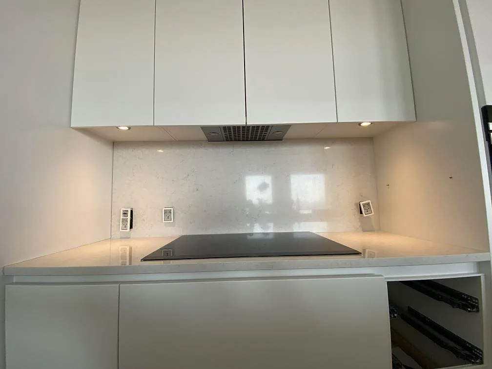 Bänksträcka i polerad Silestone Snowy Ibiza med svart häll, ljus väggbeklädnad i samma sten och arbetsbelysning i ett kök i København V.