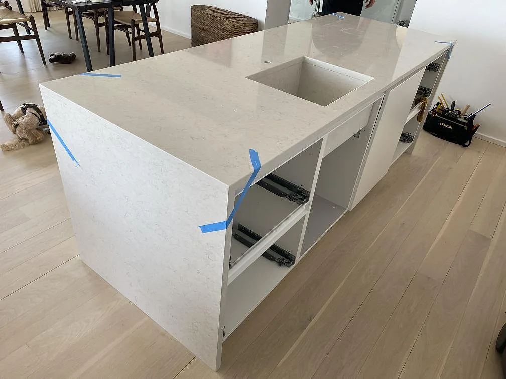 Köksö i polerad Silestone Snowy Ibiza med neddragen gavel och ljus kvartskomposit under montering i ett kök i København V.