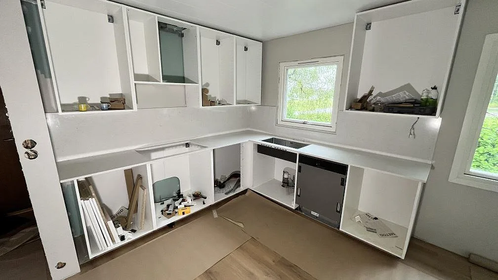 Köksbänkskiva i vit Silestone Snowy Ibiza, polerad komposit, med stänkskydd och öppna köksstommar under montering i Köping.