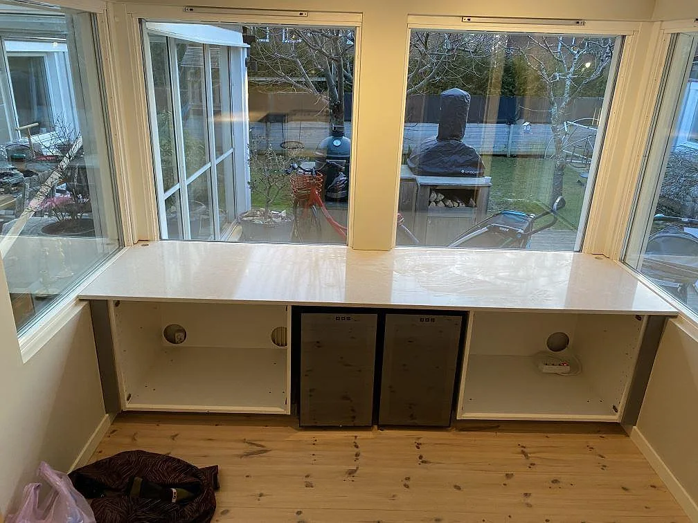 Bänk under fönster i polerad Silestone Snowy Ibiza med ljus ådring och monterade underskåp i ett kök i Kungsbacka.