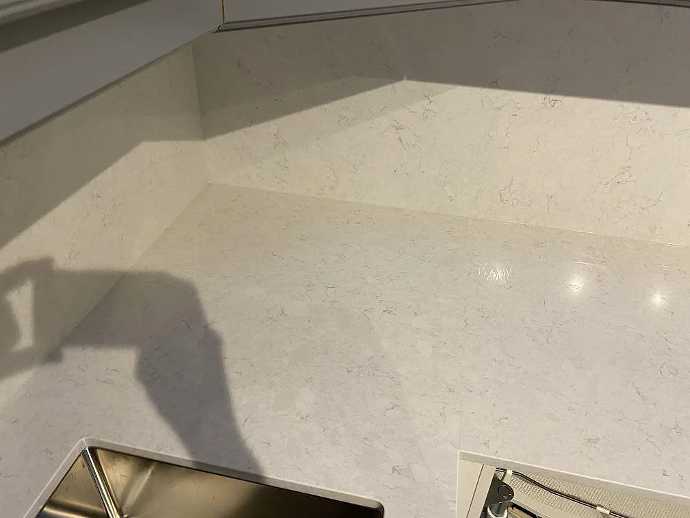 Hörnvy av köksbänkskiva i polerad Silestone Snowy Ibiza med låg stänkkant och ljus stenådring i Kungsbacka.