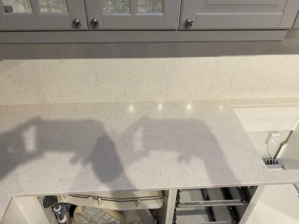 Lång köksbänk i polerad Silestone Snowy Ibiza med låg stänkkant och öppna stommar under montering i Kungsbacka.