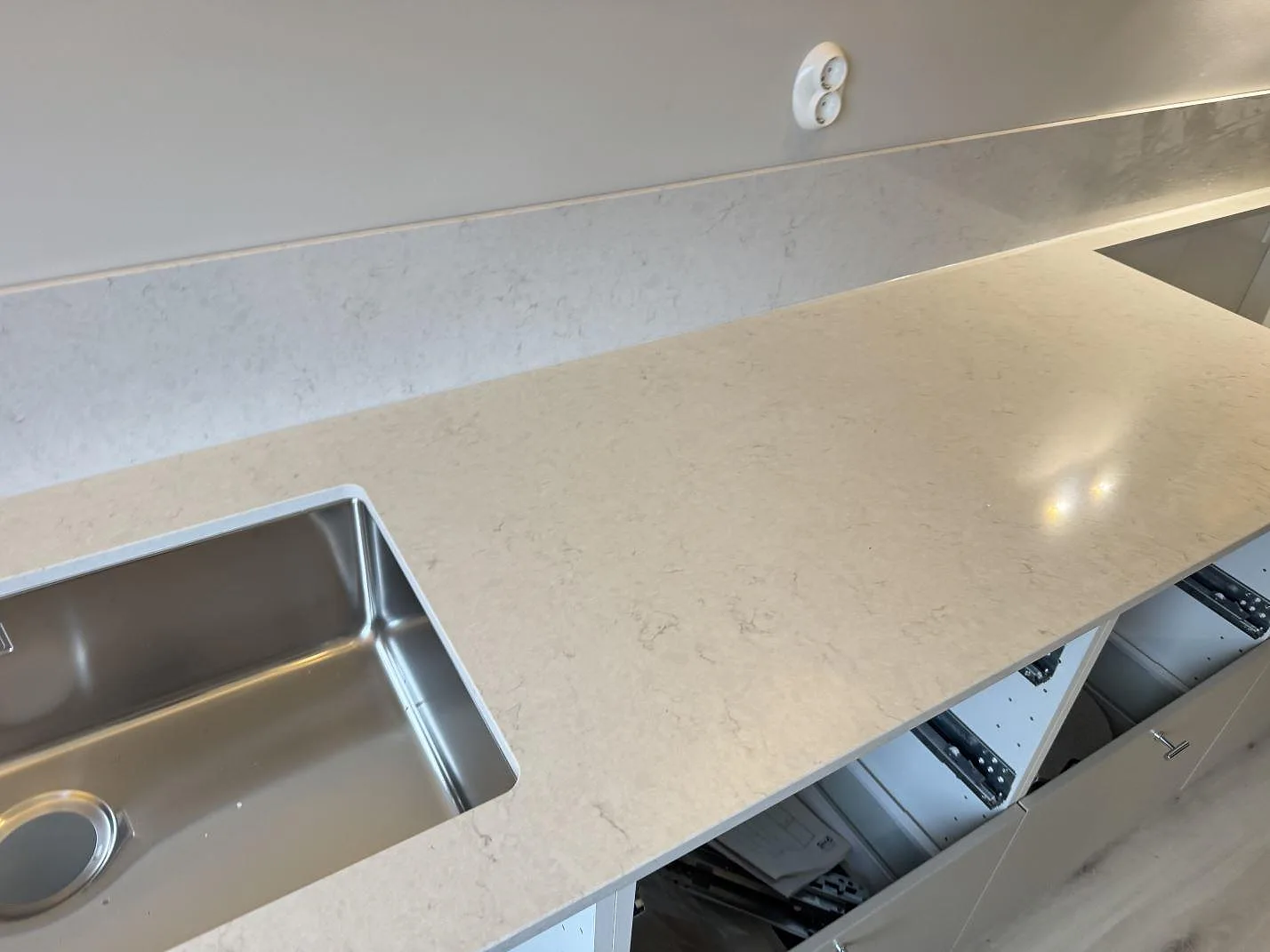 Lång rak köksbänk i polerad Silestone Snowy Ibiza med mjuk grå ådring och underlimmad rostfri ho i ett kök i Laholm.