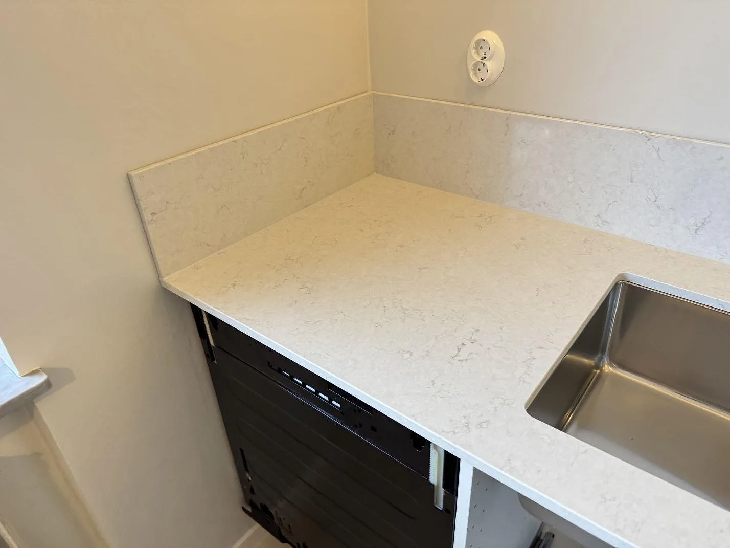 Hörn av köksbänk i Silestone Snowy Ibiza med underlimmad rostfri diskho och 12 mm stänkkant, monterad under montering i Laholm.