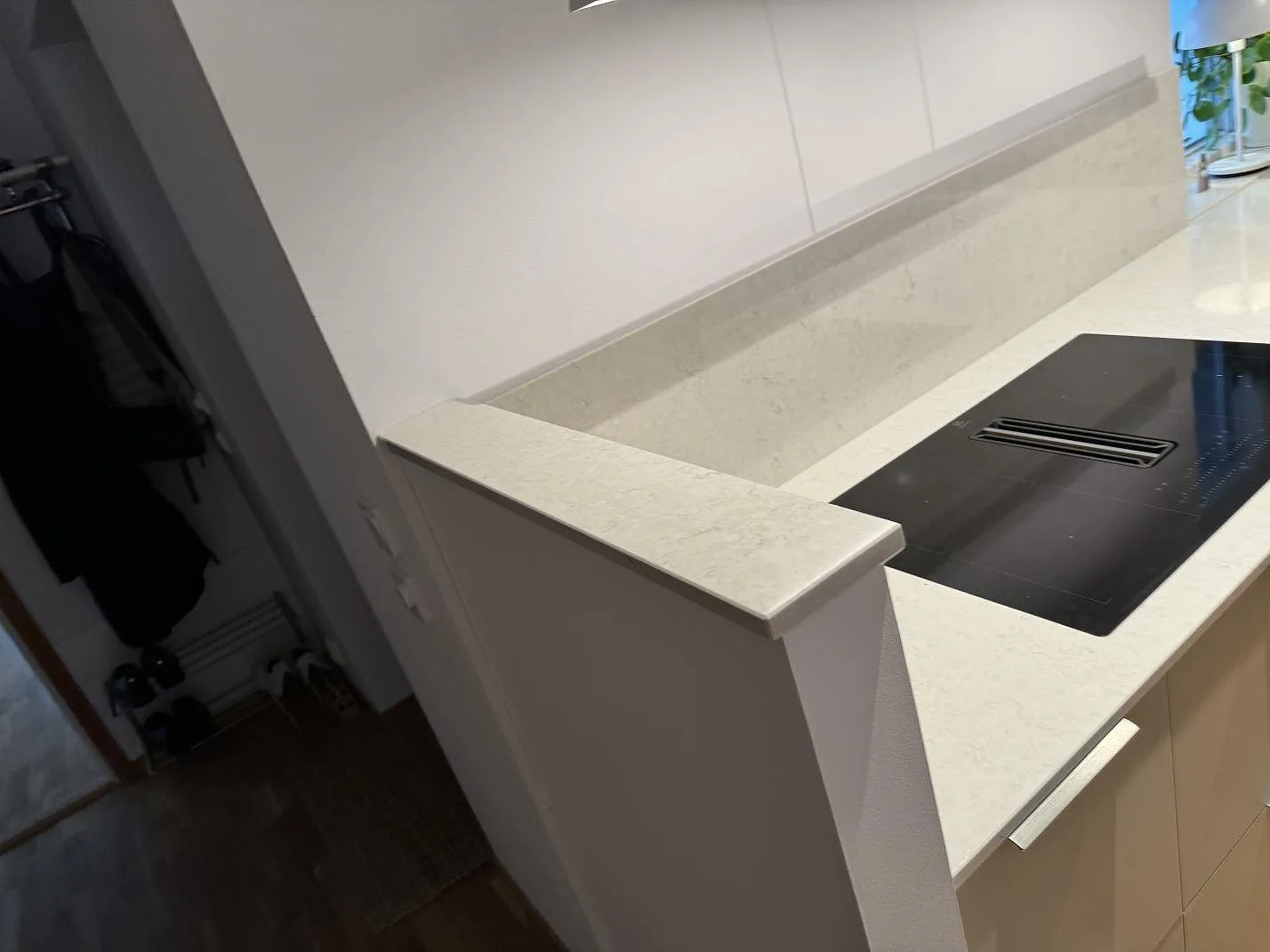 Köksbänkskiva i polerad Silestone Snowy Ibiza med induktionshäll och låg stenkant vid väggen i Landskrona.