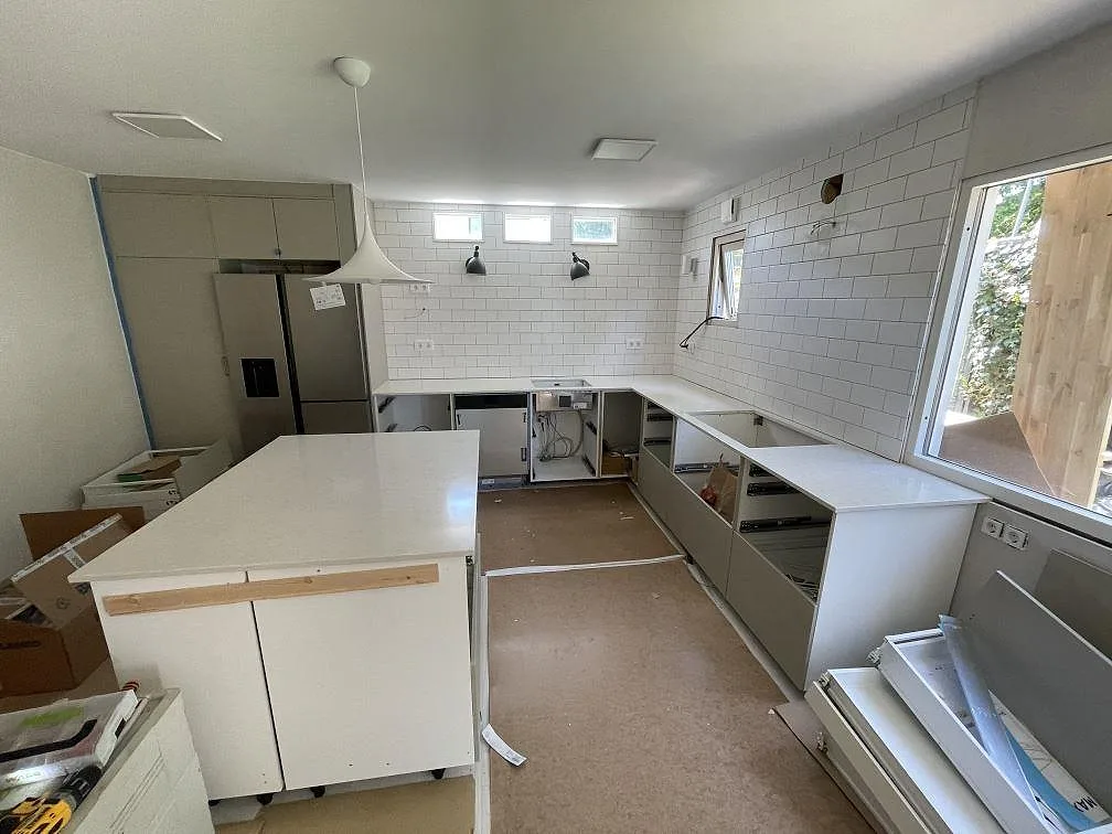 Polerad köksbänkskiva i Silestone Snowy Ibiza med köksö och väggbänkar i ett vitt kök under montering i Landvetter.