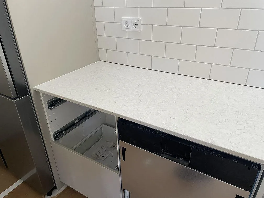 Väggbänk i polerad Silestone Snowy Ibiza ovanför diskmaskinsplats och vita stommar i Landvetter.