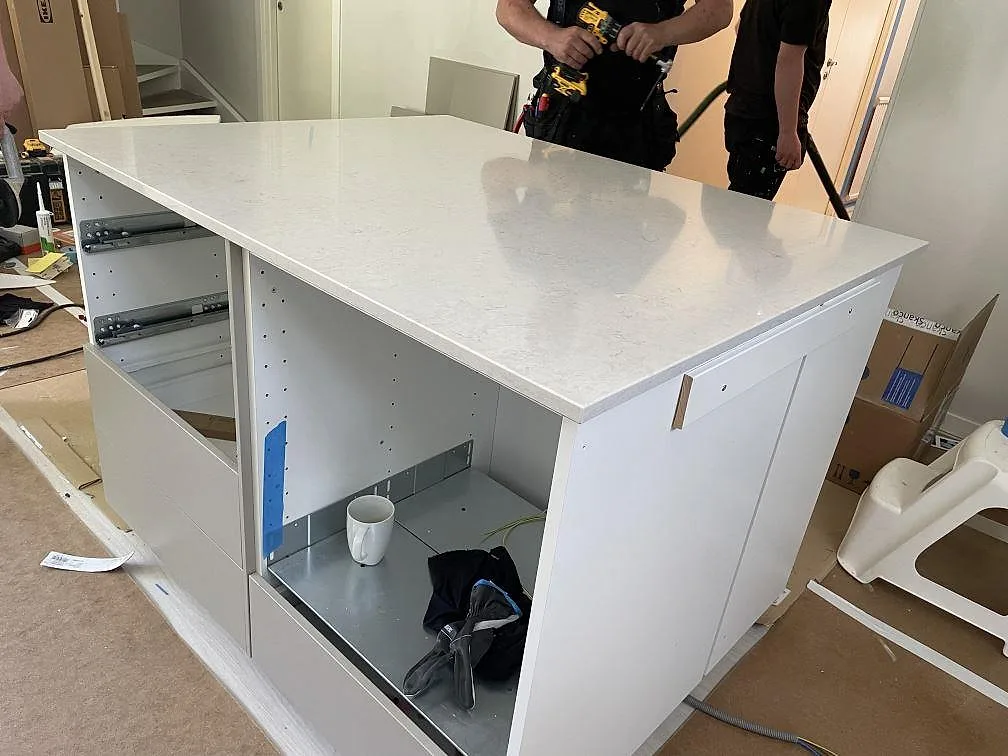 Köksö i polerad Silestone Snowy Ibiza, vit komposit, med installatörer i bakgrunden under montering i Landvetter.