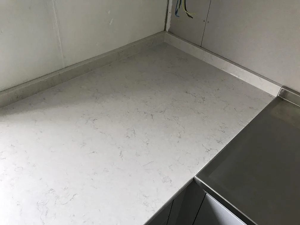 Polerad bänkskiva i Silestone Snowy Ibiza i en köksvinkel med synliga väggar och rostfri häll intill, under montering i ett kök i Lerum.