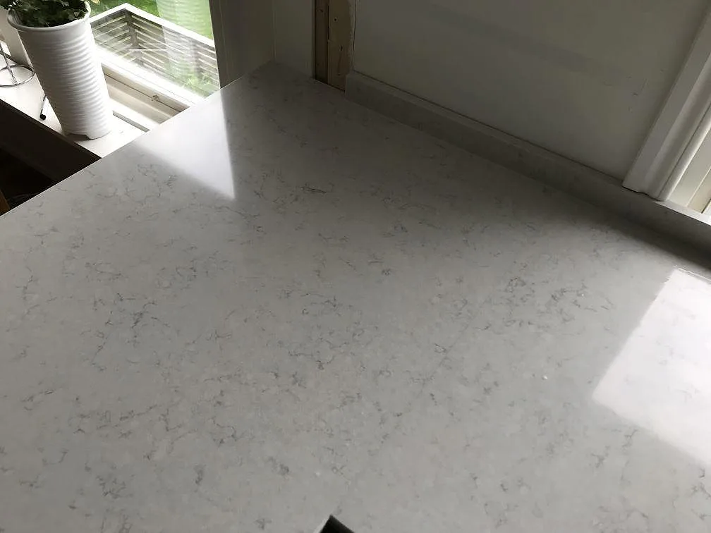 Köksbänkskiva i Silestone Snowy Ibiza vid fönstret med krukväxt, polerad vit kvartskomposit i ett kök i Lerum.