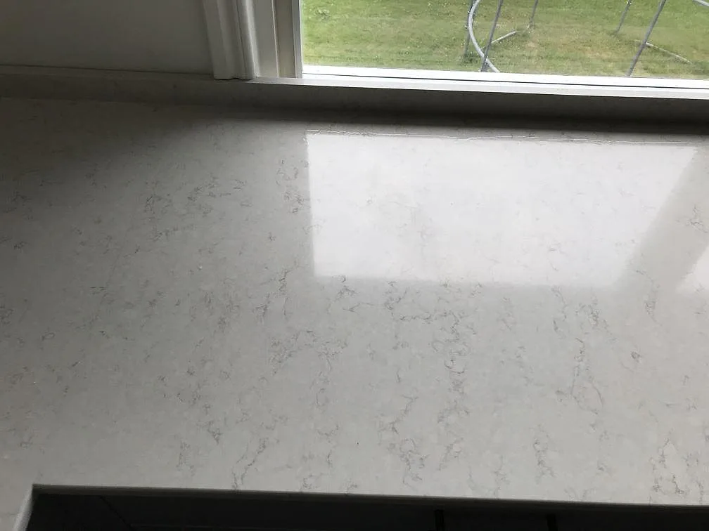 Polerad fönsterbänk i Silestone Snowy Ibiza med fin grå ådring och spegling från fönstret i ett kök i Lerum.
