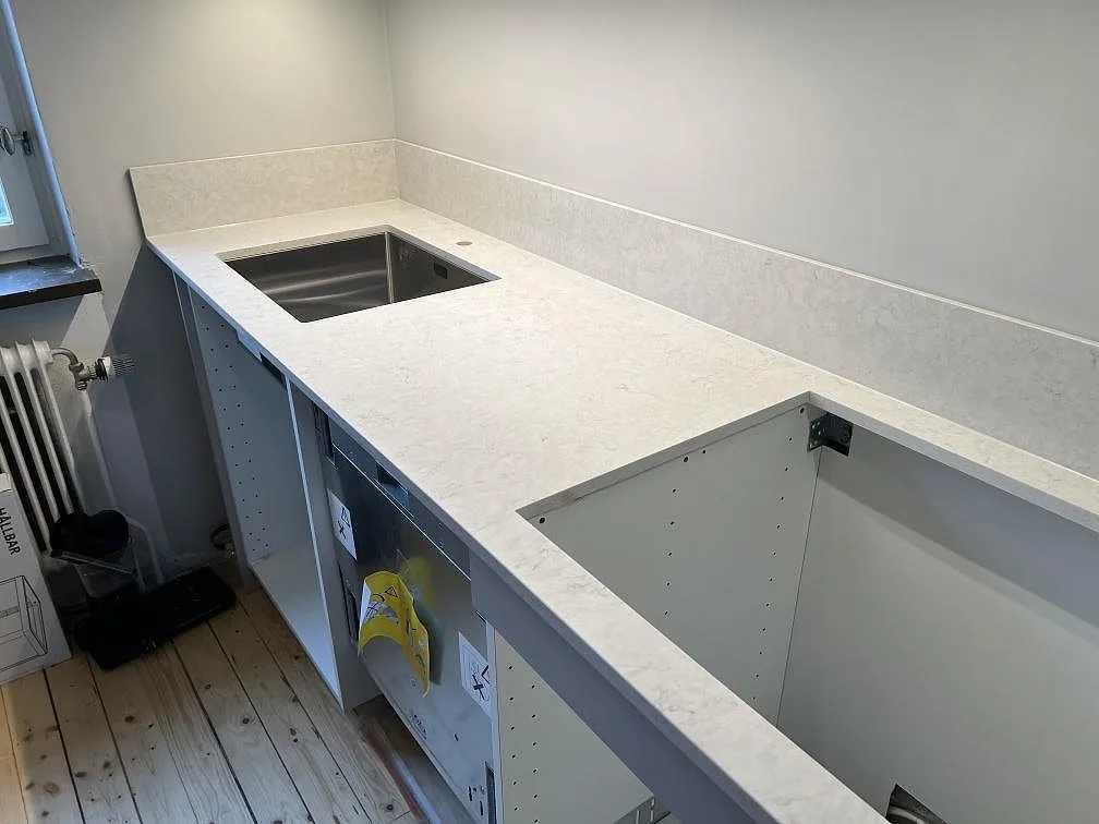 Närbild på polerad Silestone Snowy Ibiza komposit med rostfri diskho, hällurtag och låg stänkkant i ett kök i Lidingö.