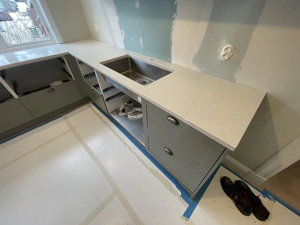Hörnparti av köksbänkskiva i vit Silestone Snowy Ibiza med underlimmad rostfri diskho i ett kök under montering i Lidingö.