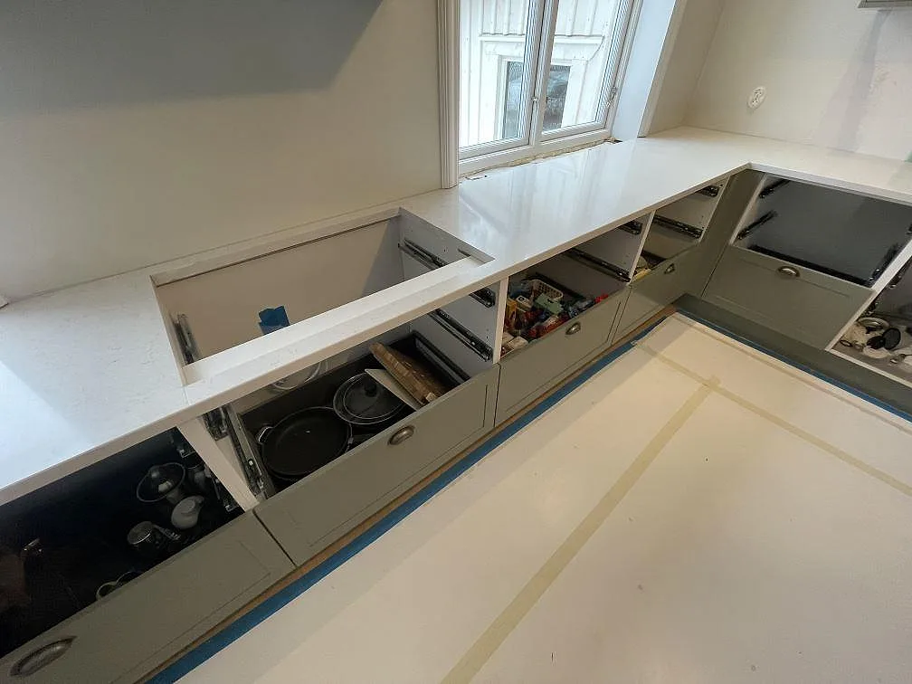 L-formad köksbänk i vit Silestone Snowy Ibiza, polerad, med utdragna lådor och fönster ovanför i ett kök i Lidingö.