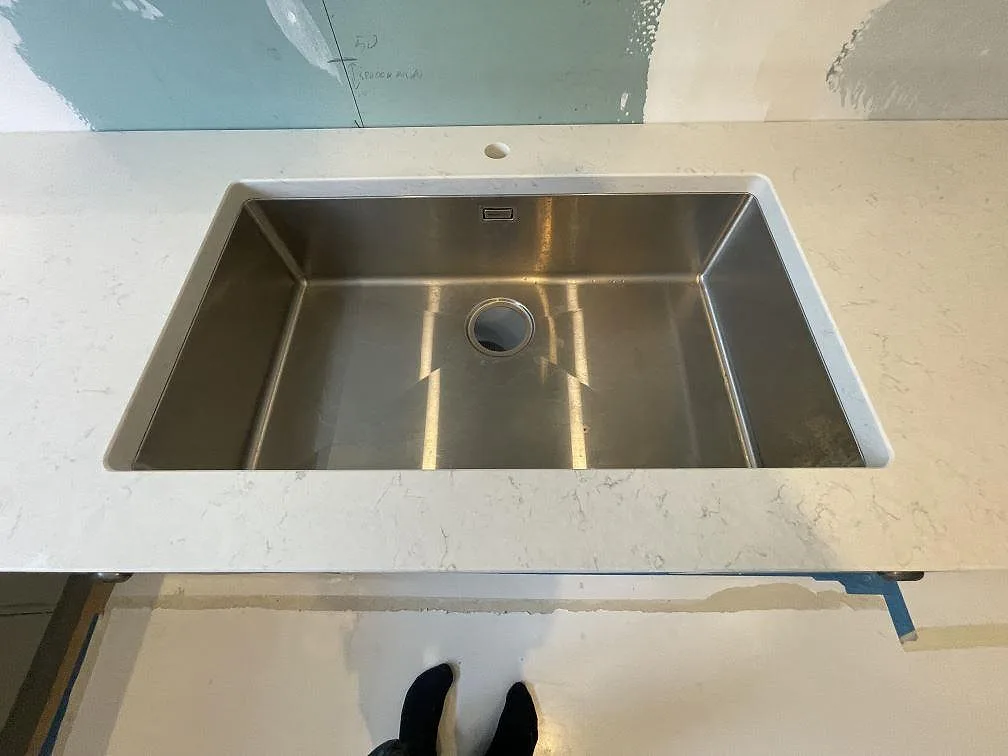 Underlimmad rostfri diskho ovanifrån i polerad vit Silestone Snowy Ibiza med synlig blandarhål och fin ådring i ett kök i Lidingö.