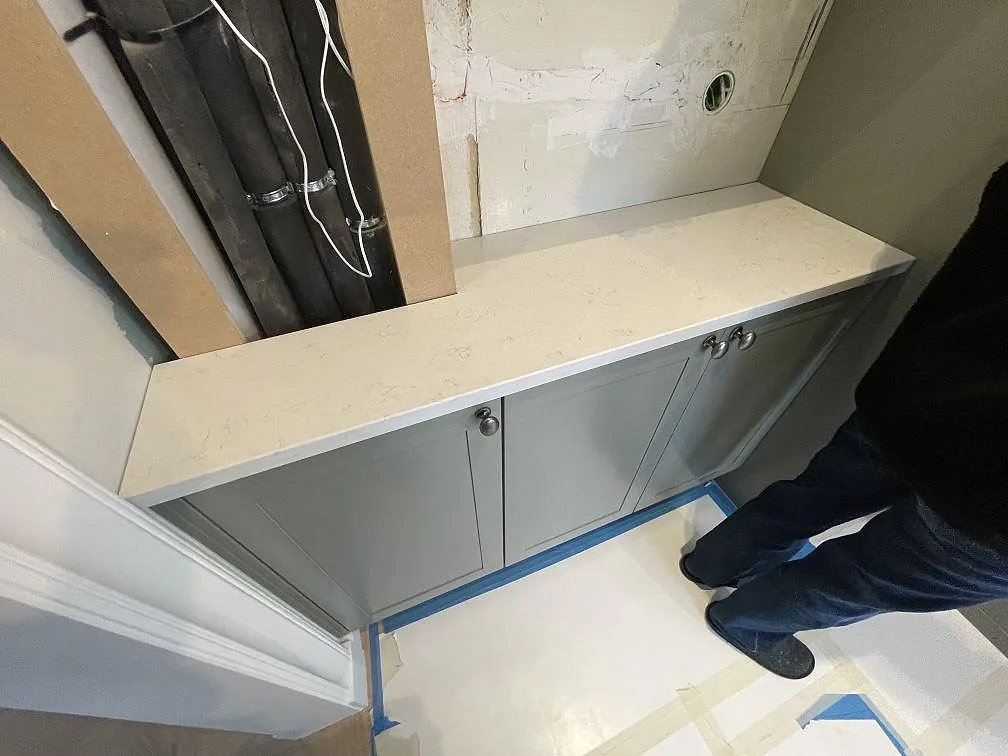 Smalt bänkparti i polerad vit Silestone Snowy Ibiza ovanpå grå underskåp i en sidodel av köket under montering i Lidingö.
