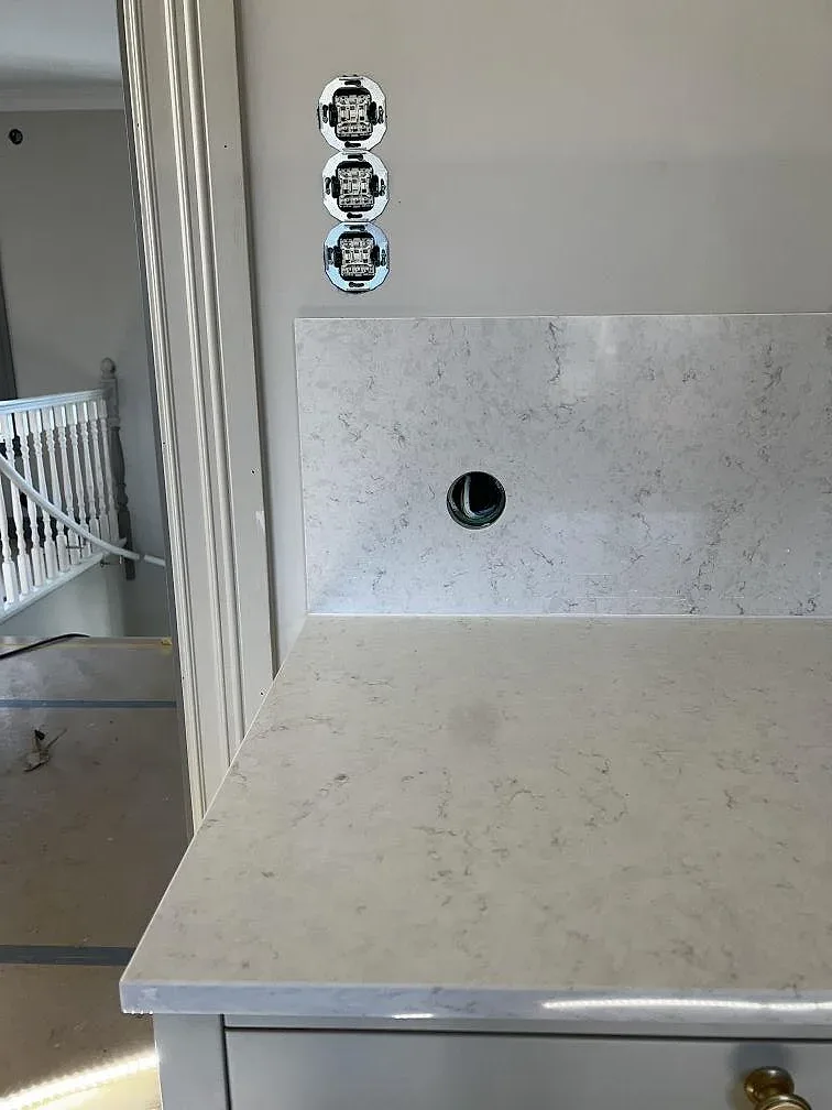 Polerad Silestone Snowy Ibiza bänkskiva med blandarhål och uppvikt stänkkant mot vägg i ett kök i Lidköping.