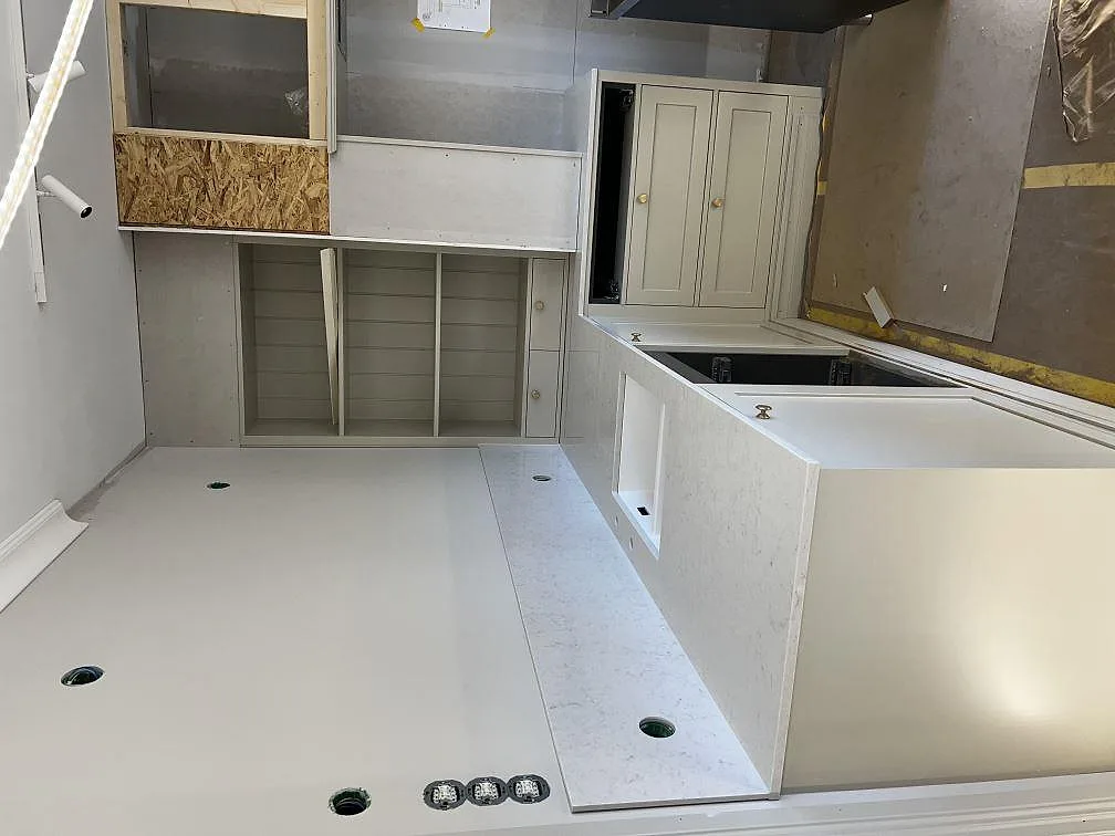 Vit Silestone Snowy Ibiza köksbänkskiva längs köksrad och halvö med krämvita ramluckor i ett kök under inredning i Lidköping.