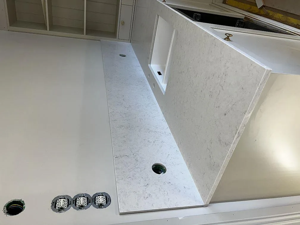 Polerad Silestone Snowy Ibiza bänkskiva på halvö med blandarhål och uppvikt stänkskydd i ett kök i Lidköping.