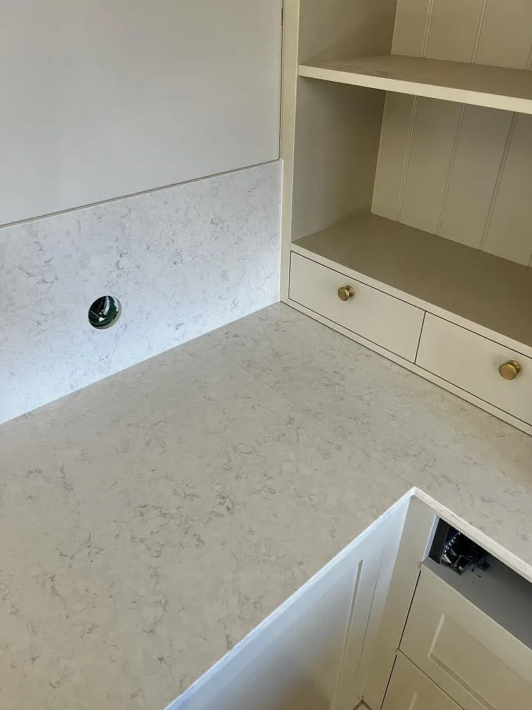 Vit Silestone Snowy Ibiza bänkskiva med blandarhål mot krämvita ramluckor med mässingsknoppar i ett kök i Lidköping.