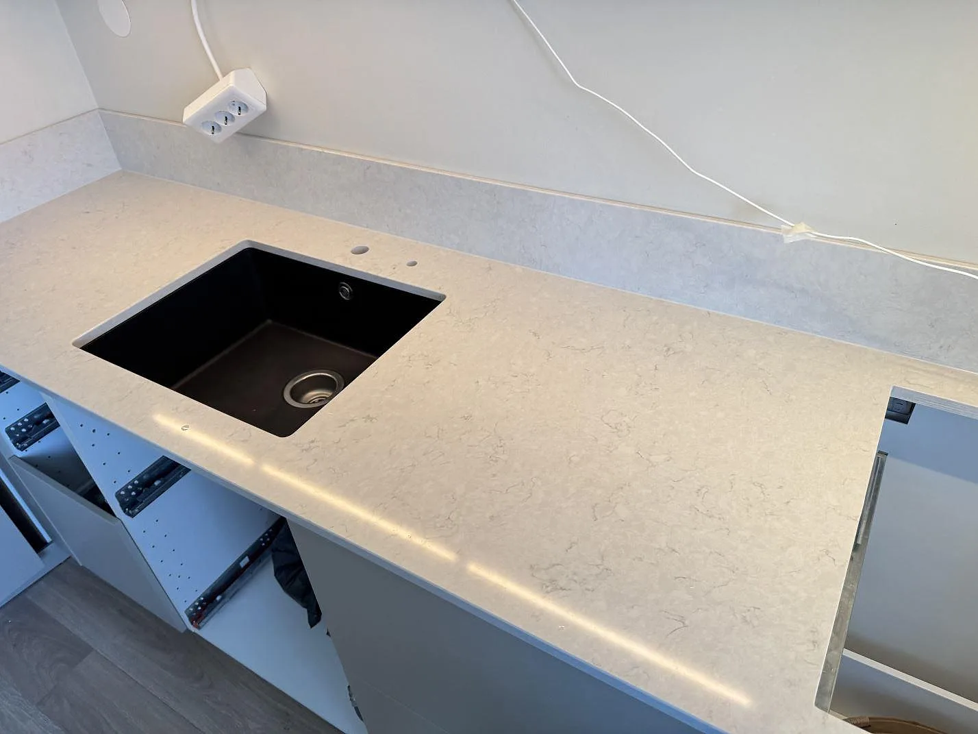 Polerad bänkskiva i Silestone Snowy Ibiza med svart diskho, blandarhål och förberett hällurtag i ett kök i Lidköping.