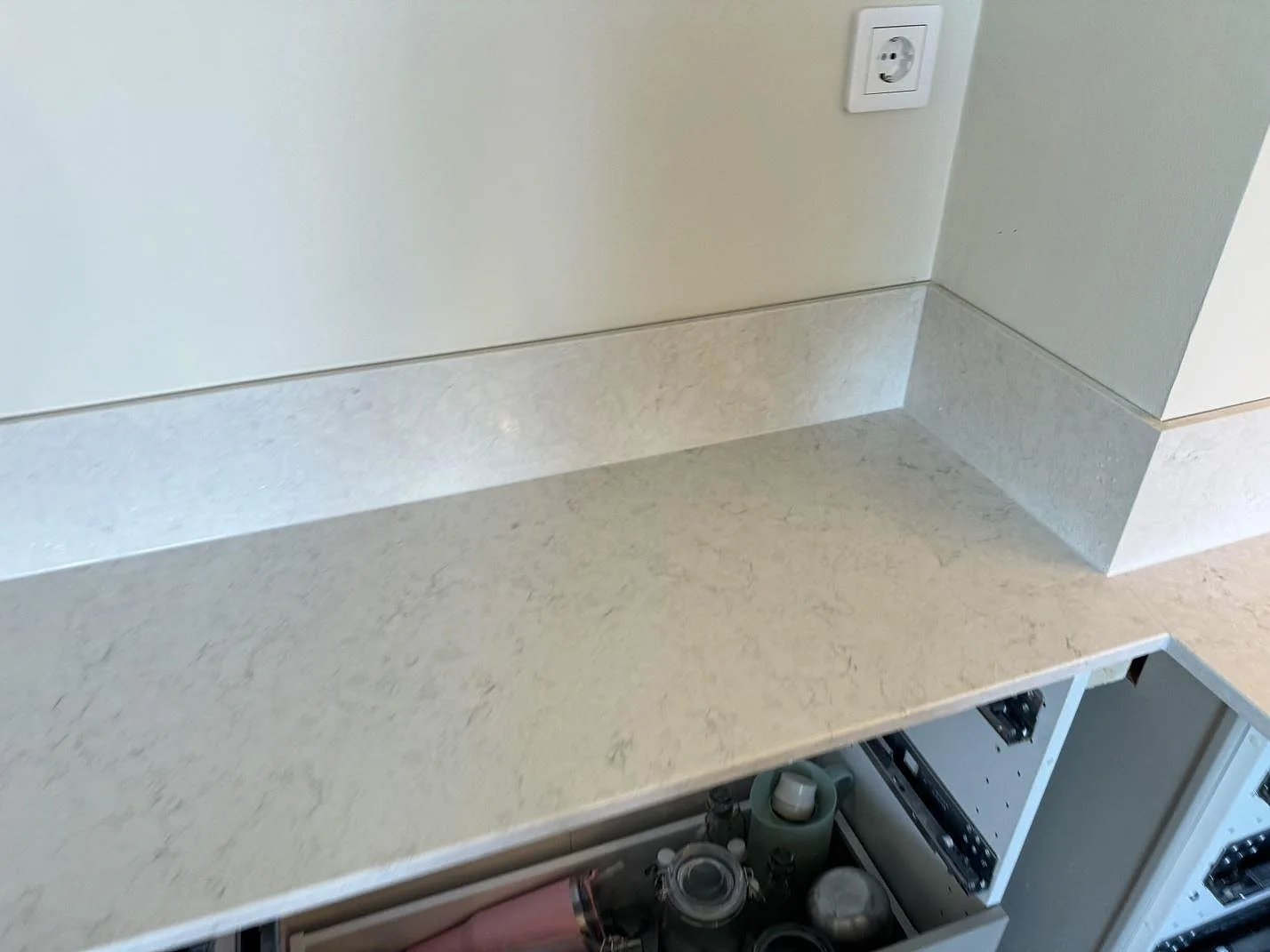Ljus Silestone Snowy Ibiza bänkskiva med uppvikt stänkkant runt ett invändigt hörn i ett kök i Lidköping.