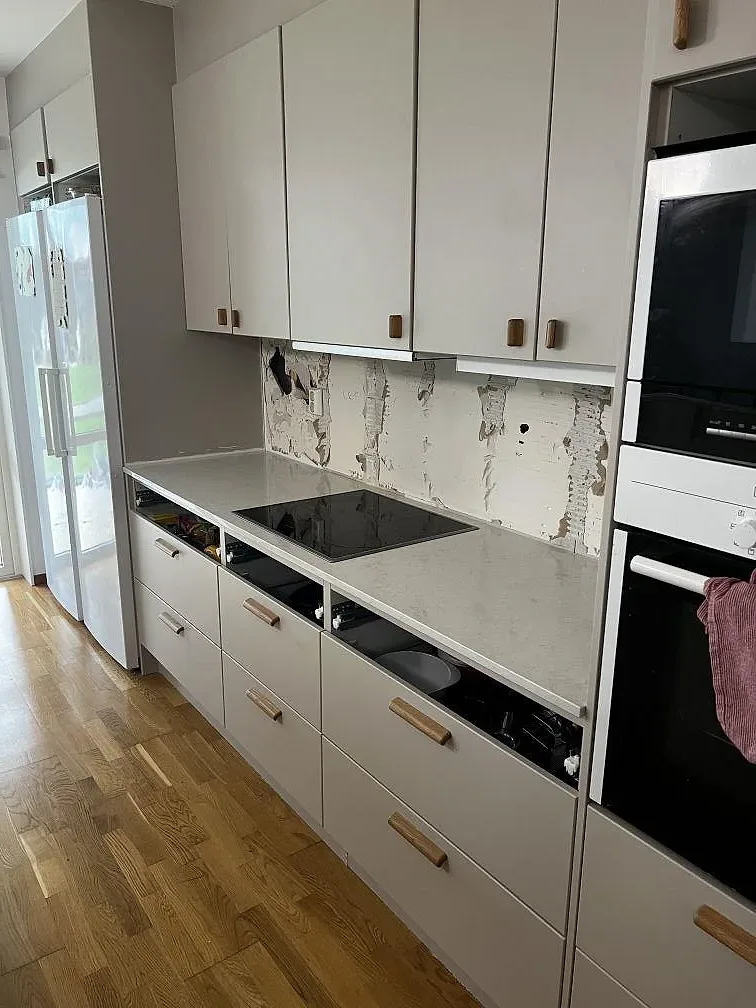 Polerad Silestone Snowy Ibiza som L-formad köksbänkskiva med svart induktionshäll och vita skåp i Limhamn.