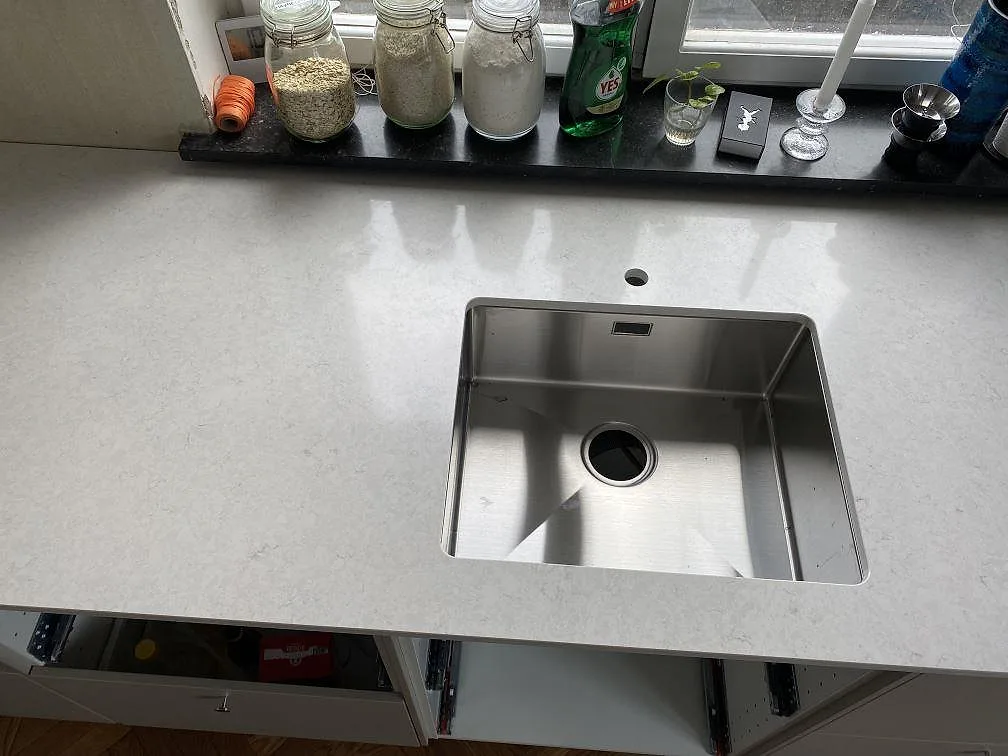 Närbild på polerad Silestone Snowy Ibiza runt en rostfri diskho monterad under stenen i Limhamn.