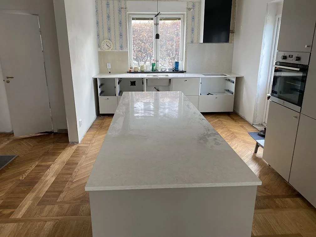 Köksbänkskiva och köksö i polerad Silestone Snowy Ibiza, vit kvartskomposit, under montering i ett kök i Limhamn.