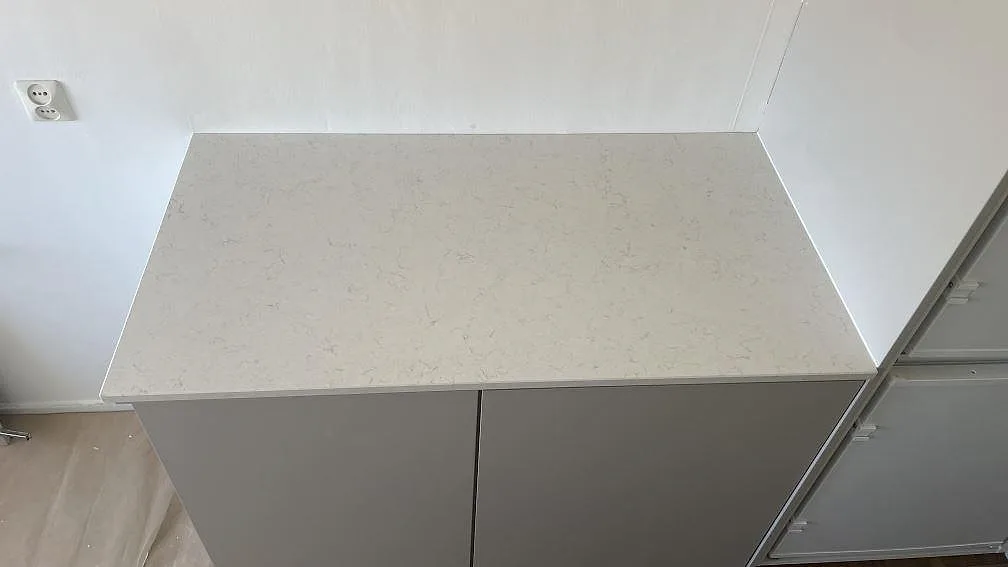 Sidobänk i 20 mm polerad Silestone Snowy Ibiza med ljus ådring mot vägg i ett kök under montering i Limhamn.