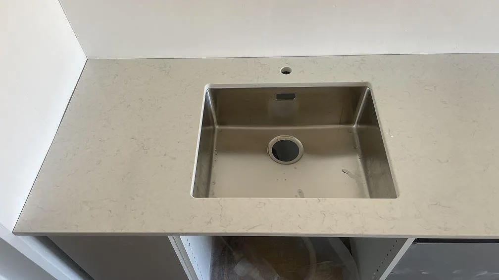 Underlimmad rostfri diskho i en 20 mm polerad Silestone Snowy Ibiza-bänkskiva med kranhål bakom i ett kök i Limhamn.