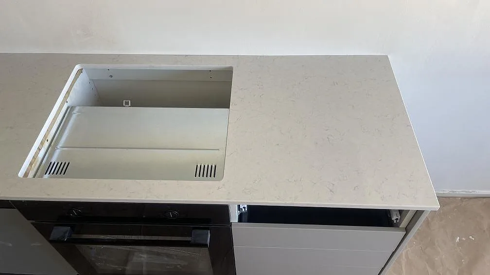 Hällurtag i en vit polerad Silestone Snowy Ibiza-bänkskiva ovanför ugn i ett kök under montering i Limhamn.
