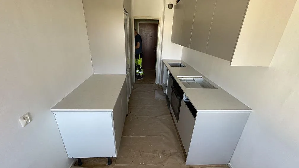 Köksbänkskiva i vit polerad Silestone Snowy Ibiza i ett smalt kök i Limhamn, med underlimmad rostfri diskho och hällurtag under montering.