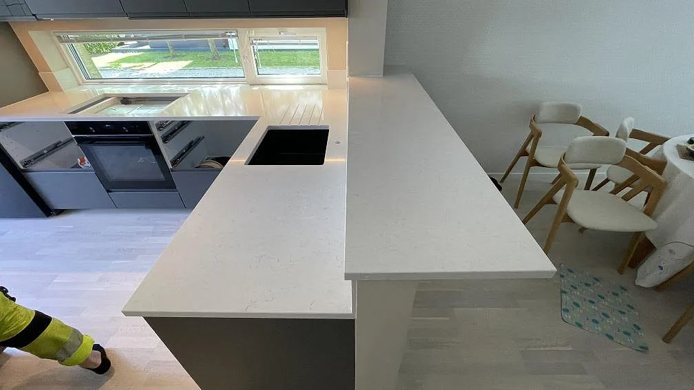 Polerad Silestone Snowy Ibiza som arbetsyta på halvö och väggbänk, ljus kvartskomposit med öppna stommar under montering i Limhamn.