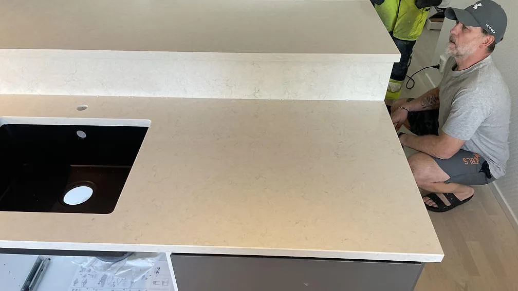 Detalj av polerad Silestone Snowy Ibiza bänkskiva under montering, med mörk ho och ljus sten på halvön i Limhamn.
