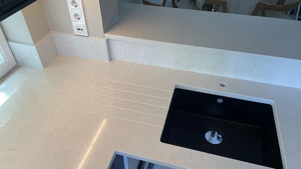 Köksbänk i polerad Silestone Snowy Ibiza med mörk diskho, avrinningsspår och ljusa stänkpartier vid väggen i Limhamn.