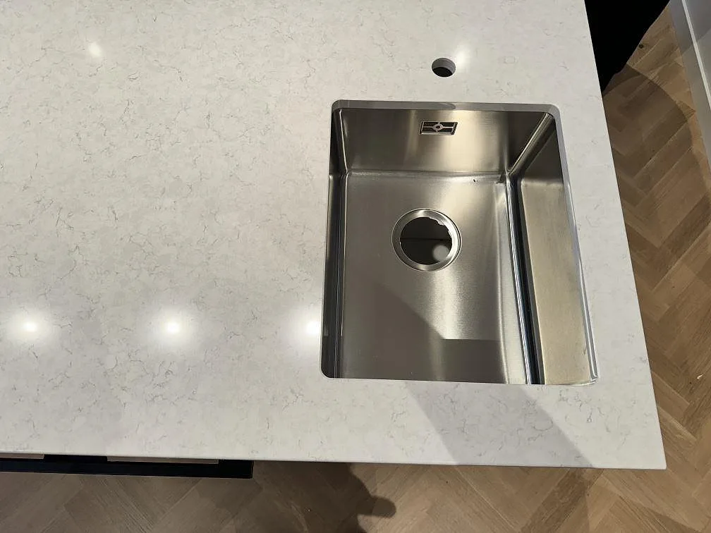 Närbild ovanifrån av rostfri diskho i polerad Silestone Snowy Ibiza med vitgrå mönstring i köket i Lindome.