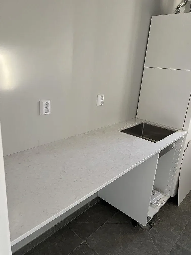 Köksbänkskiva längs väggen i polerad Silestone Snowy Ibiza, ljus kvartskomposit, med förberedd öppning och öppna köksstommar i Ljusterö.
