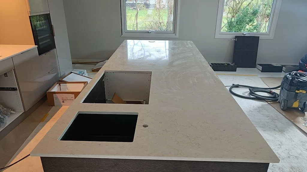 Polerad köksö i Silestone Snowy Ibiza med svart diskho, blandarhål och öppna köksstommar under montering i Löddeköpinge.