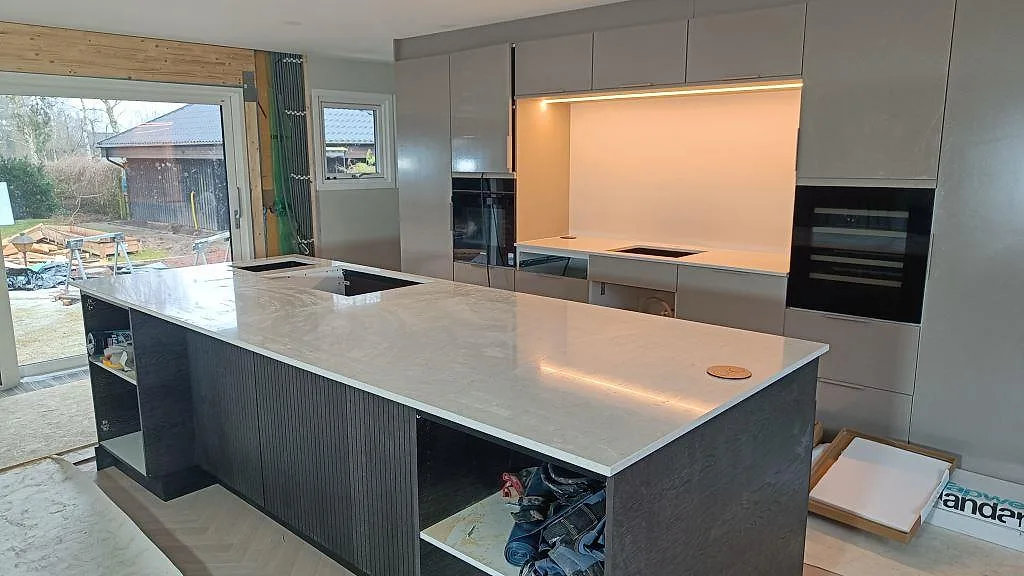 Stor köksö i 20 mm polerad Silestone Snowy Ibiza, ljus kvartskomposit med diskho och hällurtag i ett kök i Löddeköpinge.