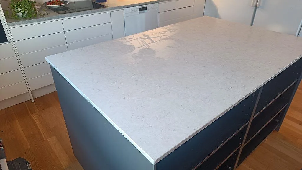 Polerad köksö i Silestone Snowy Ibiza, 20 mm ljus kvartskomposit, fotograferad från sidan med vita köksskåp i Löddeköpinge.
