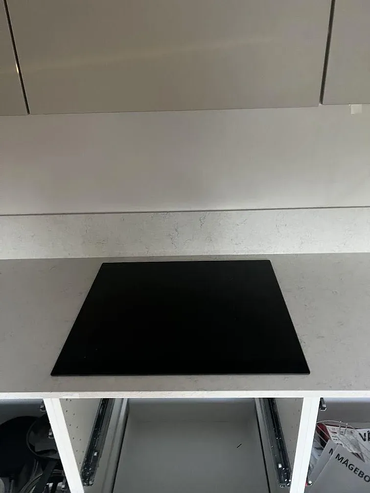 Svart induktionshäll monterad i polerad Silestone Snowy Ibiza bänkskiva med öppna vita stommar i Lomma.