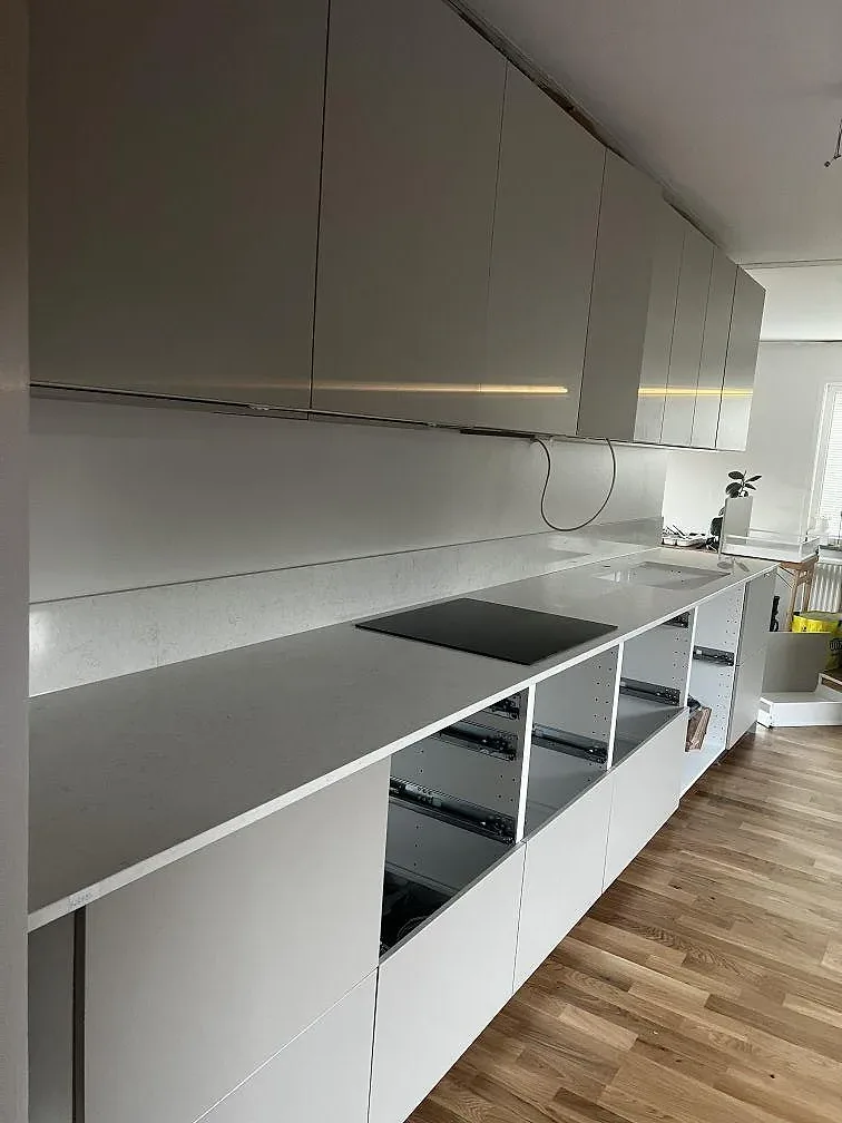 Lång köksbänkskiva i polerad Silestone Snowy Ibiza med svart induktionshäll och vita skåpstommar i ett kök i Lomma.