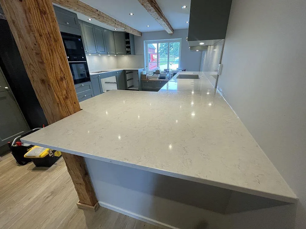 Köksbänkskiva i polerad Silestone Snowy Ibiza komposit med halvö, grå köksinredning och synlig träbjälke i Ludvigsborg.