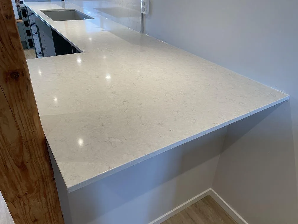 Halvö med polerad Silestone Snowy Ibiza komposit, ljus ådring och svart häll i ett kök i Ludvigsborg.