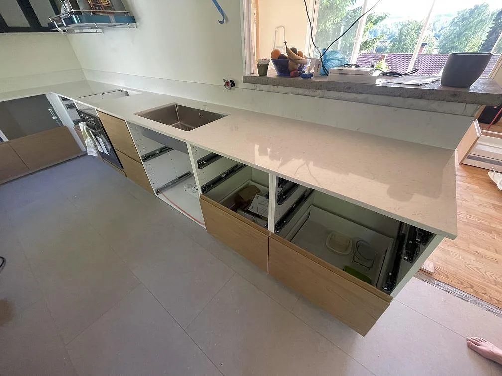 Närmare bild av den polerade Silestone Snowy Ibiza-bänkskivan med rostfri diskho, hällurtag och öppna köksstommar i Ludvika.