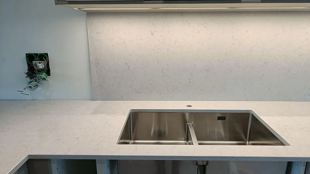 Polerad Silestone Snowy Ibiza köksbänkskiva i Lund med dubbel underlimmad rostfri diskho och en heltäckande stänkvägg i samma sten.
