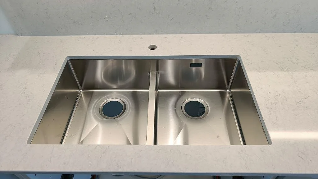 Närbild på en dubbel rostfri underlimmad diskho infälld i en polerad Silestone Snowy Ibiza bänkskiva i ett kök i Lund.