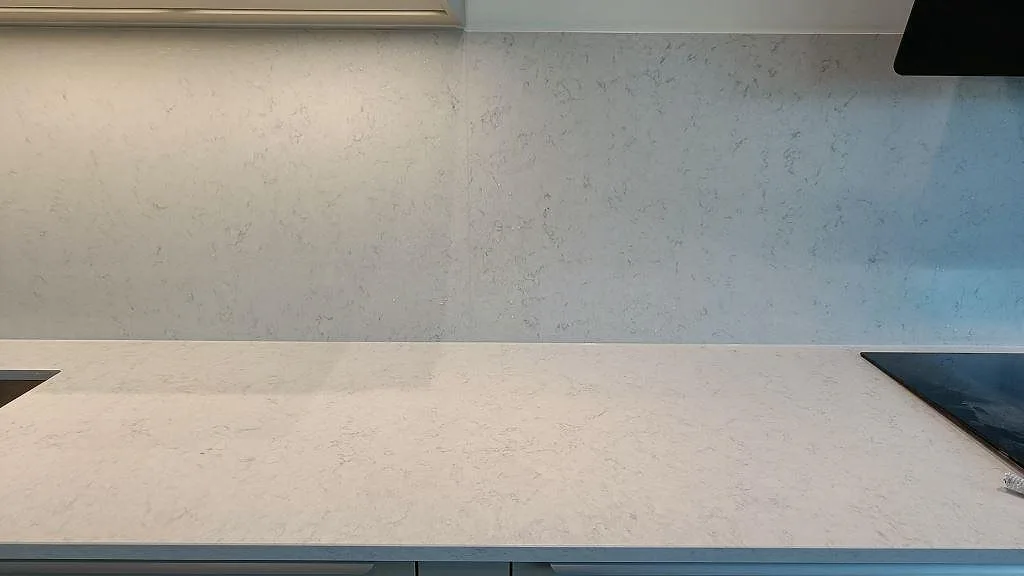 Köksbänkskiva i polerad Silestone Snowy Ibiza i Lund med inbyggd induktionshäll och en hög stänkvägg i samma vita komposit.
